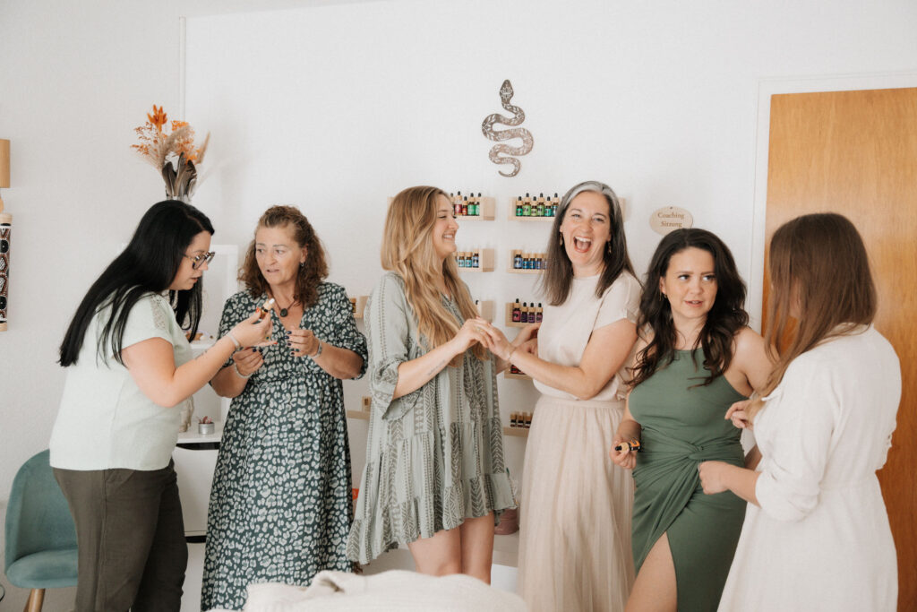 Sechs Frauen stehen vor einem ätherische Öle Regal und lachen.