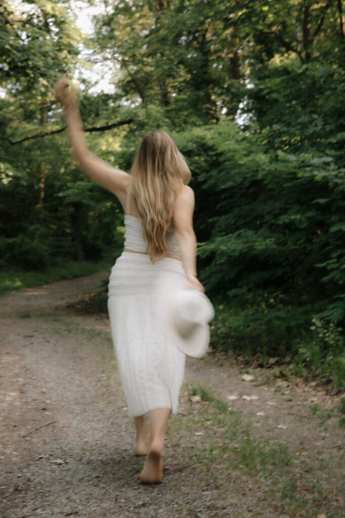 Verschwommenes Bild auf dem eine Frau in weiss gekleidet mit Hut barfuss durch Wald läuft