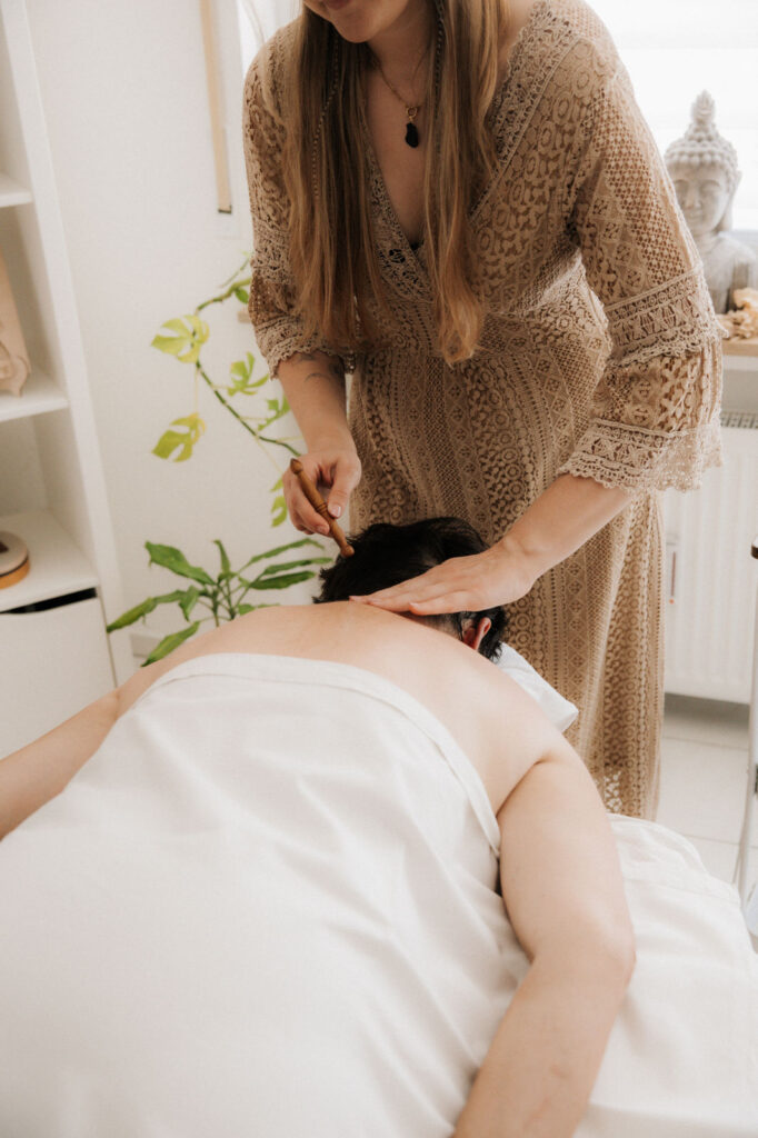 Eine Frau steht und gibt mit einem Griffel einer anderen Frau eine Aromaakupressur.